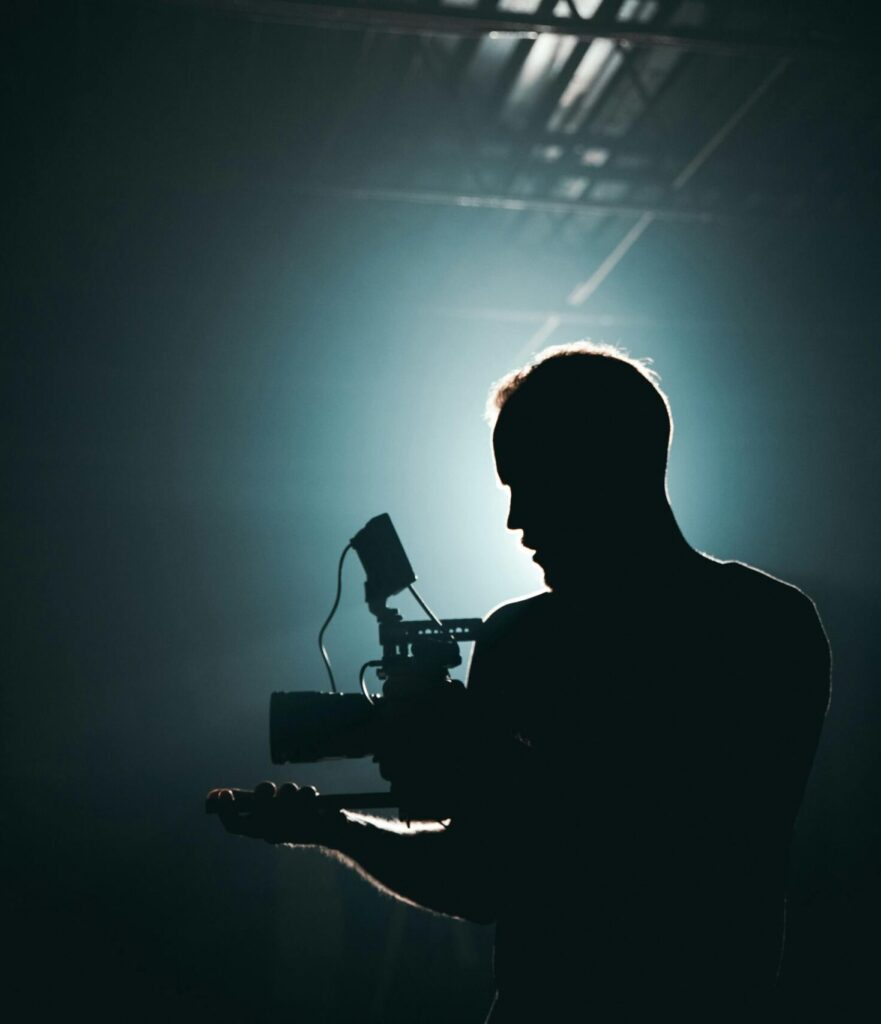 pexels-photo-3379934-3379934 Silhouette of a cinematographer with camera gear in a dramatic, low light setting.