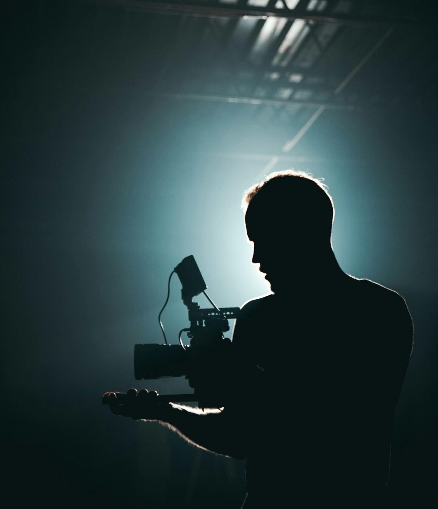 Silhouette of a cinematographer with camera gear in a dramatic, low light setting.